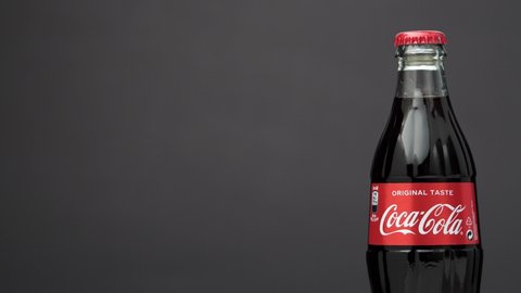 Estonia, Tallinn - March 2021: glass bottle coca-cola drink rotating on isolated dark black background. Sparkling coca-cola soda rotating 360 degree, closeup wit copy space