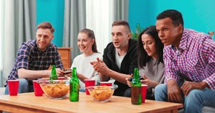 Multiethnic people celebrate video game victory in home living room. Diverse friends enoying beer and chips. Excited friends playing video games at home and having fun