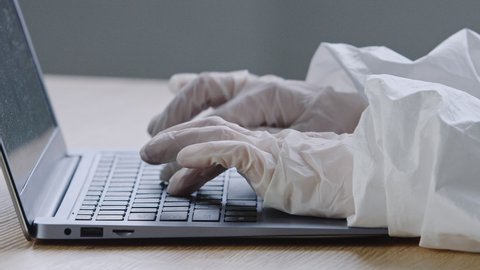 Unrecognizable doctor nurse practitioner surgeon hands typing at keyboard wears surgical medical latex gloves during coronavirus lockdown, rubber-gloved arms working with laptop in clinic close up