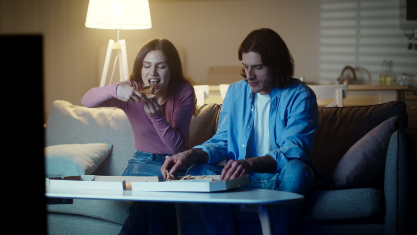 Food delivery service. Lazy young couple spending evening together, watching tv and eating hot fresh pizza, slow motion Royalty-Free Stock Footage #1073296262