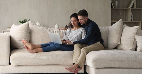 Couple sit on couch using laptop buy goods services on internet, planning vacation buy tickets booking hotels, enjoy easy comfort e-banking app. Comfort usage of modern tech e-commerce clients concept