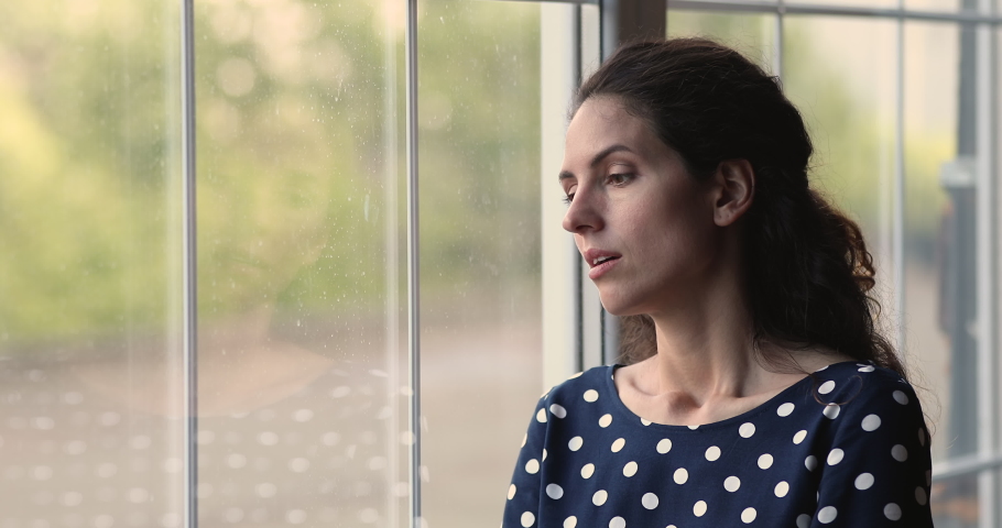 Pensive young 25s woman standing near window, thinking of life troubles or considering personal problems solution, suffering from psychological pressure, feeling doubtful about decision indoors. Royalty-Free Stock Footage #1073311784