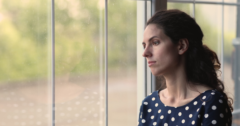 Pensive young 25s woman standing near window, thinking of life troubles or considering personal problems solution, suffering from psychological pressure, feeling doubtful about decision indoors. | Shutterstock HD Video #1073311784