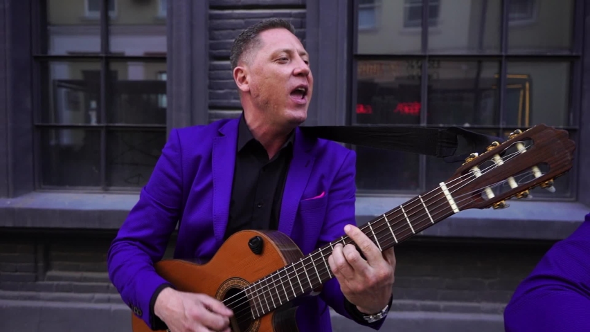 Caucasian and latin musicians play acoustic guitars in the street. Slow motion