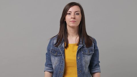 Excited jubilant overjoyed happy beautiful brunette woman 20s years old in denim jacket yellow t-shirt doing winner gesture celebrate clenching fists say yes isolated on grey color background studio
