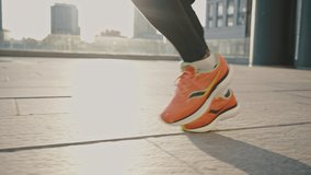 Marathon training. Close up of african american athlete in orange sneakers running in urban area, tracking shot