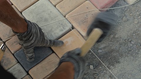 4K Details with hands of a mason working with cobble or cobblestone . Construction worker laying paving slabs on street. Engineer on protective gloves makes the sidewalk , hitting stone with hammer 
