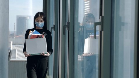 Young woman at the window in the office, loses her job, holding personal belongings in a box, quit her job, fired because of the crisis.Slow motion