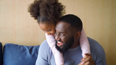 Closeup funny cute mix-raced kid daughter tickling cheerful young african american father sitting on sofa couch. Happy positive single family enjoy leisure lifestyle together have fun and play