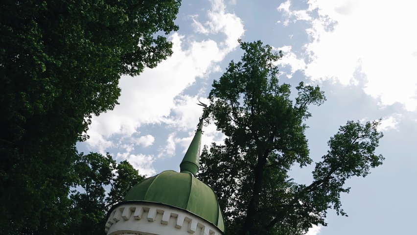 A large rounded green dome of a christian church with a long spire. Shooting through tree branches