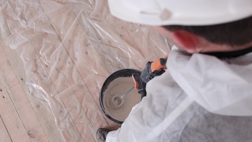 A man in a protective suit and helmet mixes cement in a bucket. The concept of renovation in the house.