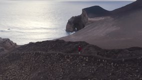 Capelinhos Volcano, Faial Island, Azores, Portugal. Aerial footage of a running man with a cave in the background. Partial view of the volcanic coast. High quality 4k footage