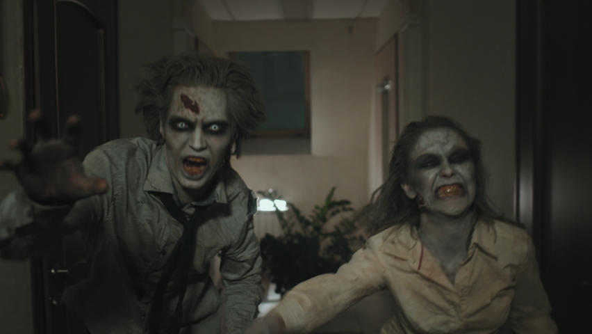 Tracking shot of creepy zombie man and woman with SFX makeup and dirty torn clothes running along dark hallway Royalty-Free Stock Footage #1073342081