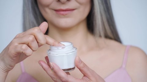 Closeup cutout portrait of mid age woman, taking face cream for older skin with fingertip. Advertising of antiwrinkle antiaging whitening rejuvenation uv protection women in menopause treatment.