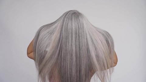 Slow motion of gorgeous middle aged mature woman, senior older 50s lady waving grey silver hair isolated on white background. Back view. Slow motion. Ads of hair care spa, hair loss prevention cure.