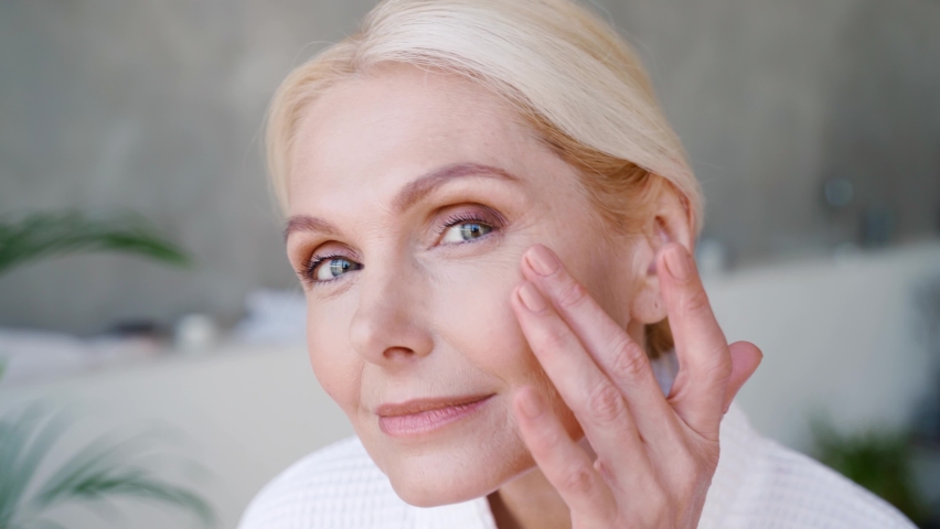 Portrait of happy smiling attractive middle aged woman wearing bathrobe touching perfect skin looking at camera. Advertising of bodycare spa procedures antiage delicate dry skin care products concept. | Shutterstock HD Video #1073342372