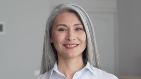Happy smiling stylish confident 50 years old Asian female professional standing looking at camera at gray background. Portrait of sophisticated grey hair woman advertising products and services. - Powered by Shutterstock - Get 15% off with code: PIKWIZARD15
