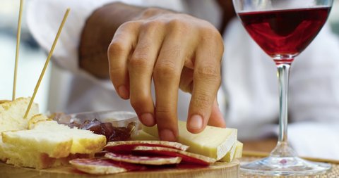 Close up of a man taking and eating french cheese, near a glass of red wine. He wears a white shirt 