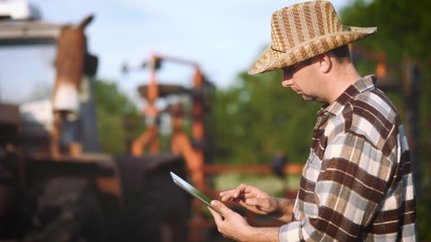 Smart farming. Farmer using digital tablet computer with tractor in the background. Man technical worker with digital tablet works next to the tractor. Concept modern technology in agriculture.