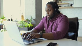 Online tutoring concept. Confident and clever African man wearing headset holding online classes webinars on the laptop,online teacher talking with student via video connect sitting in the home office