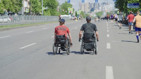 Kharkiv, Ukraine - May 16, 2021: disabled athletes on wheelchairs taking part in street race together with runners, modern buildings in the distance