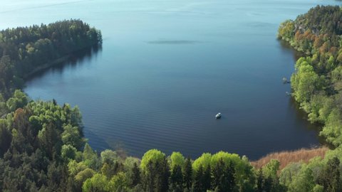 Swedish archipelago nature on sunny day in summer. Single pleasure motorboat anchoring in bay. Green forest trees at shoreline. Sweden nature at its finest. Aerial drone shot close to Stockholm