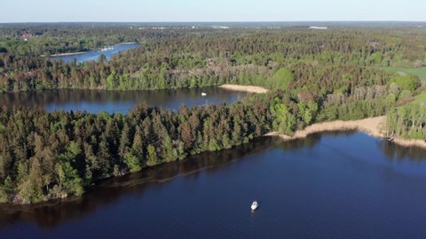Swedish Mälaren archipelago nature sunny day in summer. Single pleasure motorboat anchoring in bay. Aerial drone shot close to Stockholm.Green forest trees at shoreline. Sweden nature at its finest