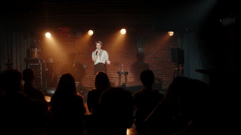 Young Caucasian female comedian performing her stand-up monologue on a stage of a small venue. Shot with ARRI Alexa Mini LF with 2x anamorphic lens