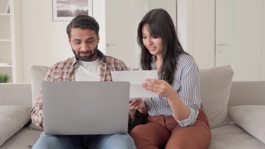 Young Indian latin family couple sitting together on sofa at home using laptop computer reading bank papers bills paying calculating loan debt taxes payments online. Wife and husband planning budget. Royalty-Free Stock Footage #1073362658