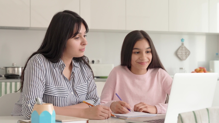 Young indian mum helping teenage daughter school girl having online video class at home sitting at kitchen table at home using laptop. Mom and kid spending time together teaching doing home work. Royalty-Free Stock Footage #1073362685