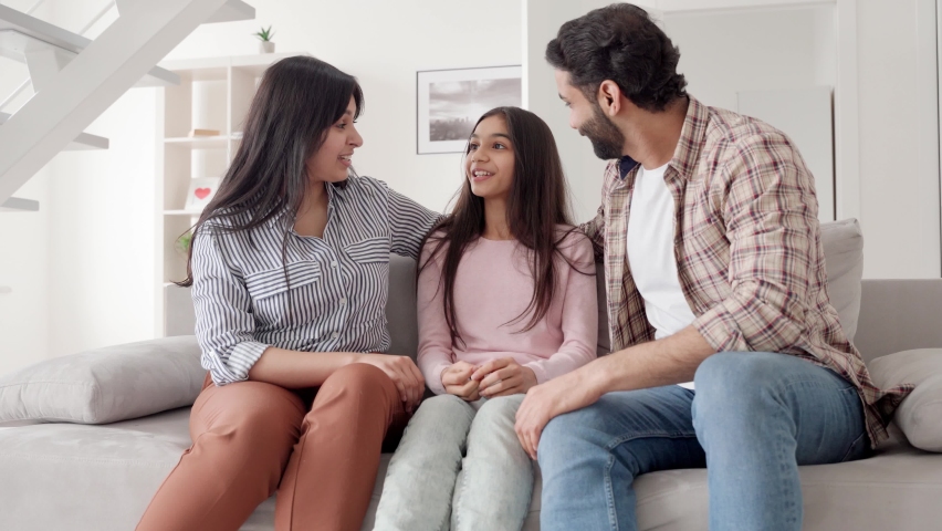 Happy family portrait. Parents listening to child daughter talking to them. Smiling laughing mom, dad and teenage kid having fun enjoying spending leisure time together at home sitting on sofa.