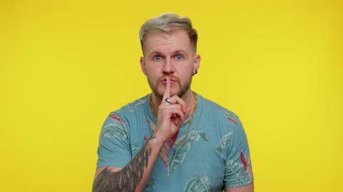 Shh be quiet please. Portrait of bearded adult guy 30 years old presses index finger to lips makes silence gesture sign do not tells secret. Young cute tourist man posing on yellow studio background