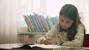 Young European girl learn home lesson. Kid write school lesson at home.