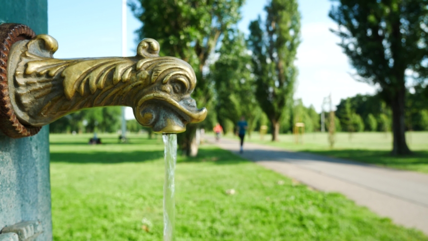 Close-up of an aged tyipical fountain with water in Milan urban green park, Italy. On the blurred background people is bicycling and jogging. Useful concept for leisure and spare time.
