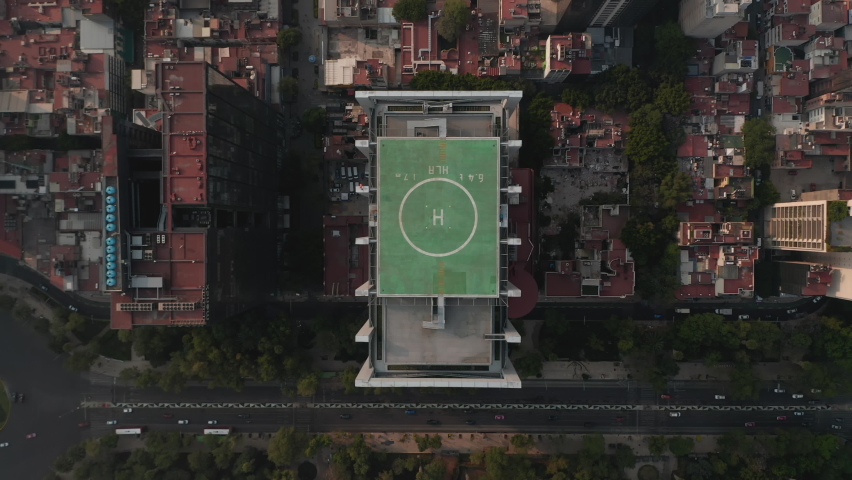 Aerial birds eye overhead top down view of tall office building with green heliport on top and surrounding area. Camera zooming out. Mexico city, Mexico.