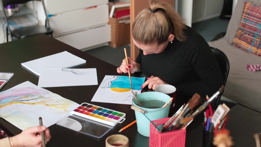 Drawing the sun. Student draws picture at table. She brushing paint on paper with brush. Displaying visual image in creative work. Creativity in art lesson. A new technique for painting with water. 