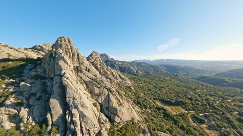 (Mountain surfing) View from above, stunning aerial video shoot by an FPV drone flying at high speed over some granite mountains and the village of San Pantaleo. Sardinia, Italy.
