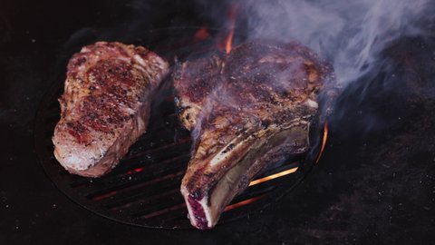 Rib eye steaks with spices on a barbecue grill grate with a blazing fire. Slow camera rotation. 4K slow motion.