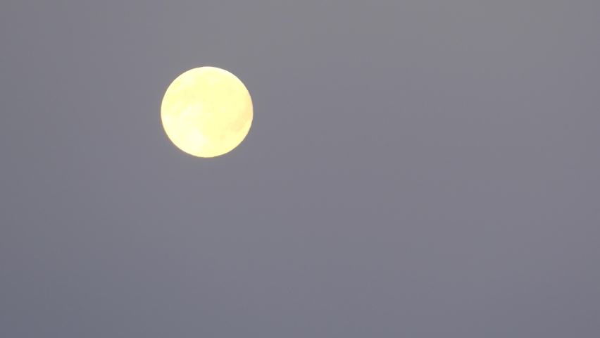 Yellow moon moving across sky. Time-lapse.