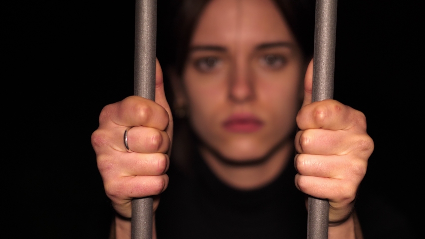 symbol of duress - sad girl clutching the bars of a gate stares at the camera Royalty-Free Stock Footage #1073377409