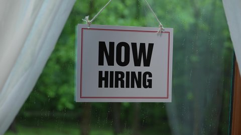 Now Hiring sign on a small business restaurant door announcing that they are now hiring.