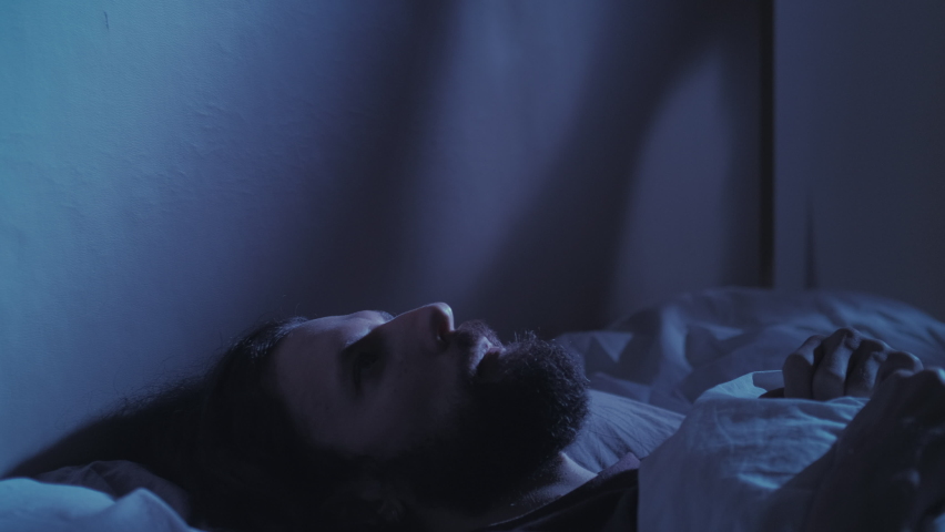 Night insomnia. Trouble sleeping. Anxiety fatigue. Tired exhausted pensive worried man overthinking lying awake alone in bed in dark bedroom with blue moonlight. Royalty-Free Stock Footage #1073379329