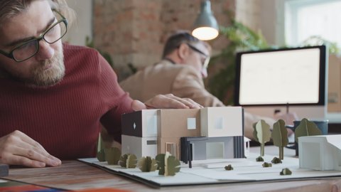 Slowmo close-up of concentrated male architect constructing 3d layout of modern building in office