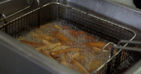 Close up French fries are fried in a pot, Process of cooking golden fried potatoes, 4k braw.