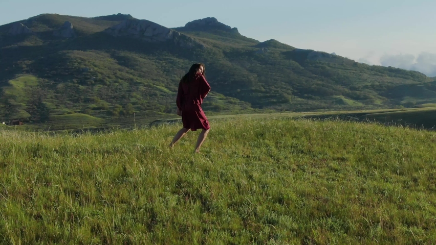Aerial view and circular panorama around a young modern shaman woman who dances a dance of power in a natural spring under a clear blue sky in the rays of the sunset