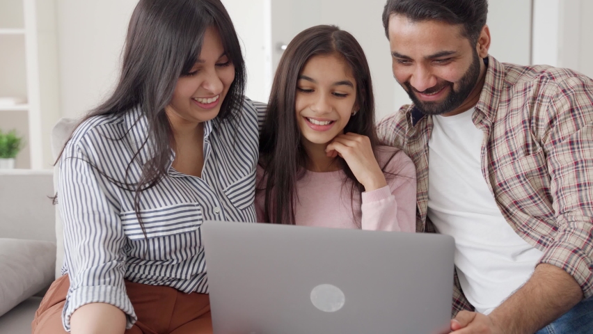 Parents with teenage daughter watching funny videos using laptop browsing online tv streaming enjoying spending time together on weekend at home in living room sitting on sofa. Happy indian family. Royalty-Free Stock Footage #1073384030