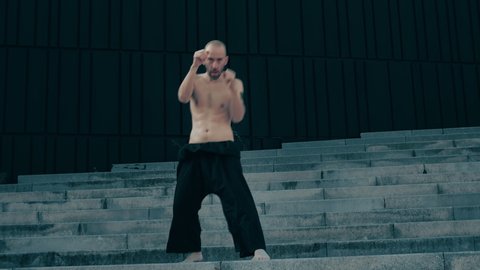 Conceptual man with tattoos training muay thai martial arts moves in urban concrete space. Strong and fit, lean athlete prepare for competition