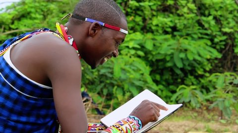 African man, laughing while reading a book, in jungle, wearing tribal gear