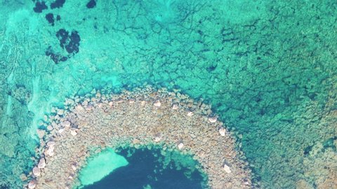 A beautiful stone path is visible through the turquoise clear sea water. Top view, shooting from a drone.