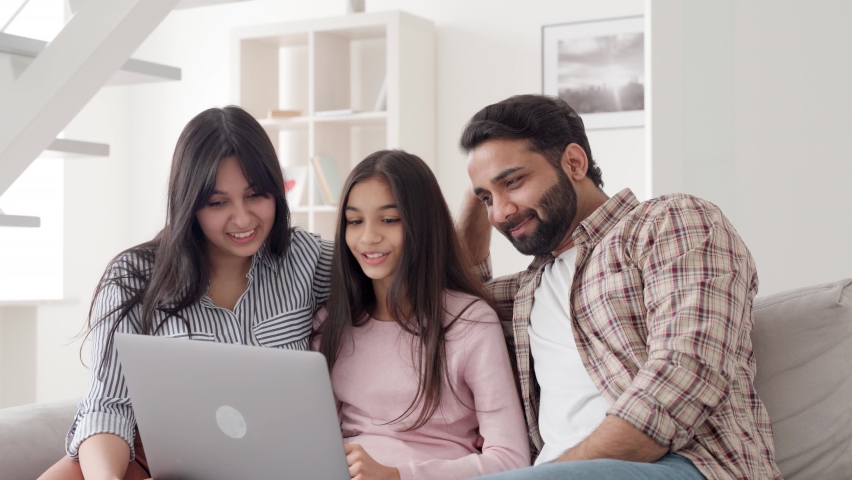 Happy family portrait. Parents with child daughter watching funny videos using laptop computer having fun enjoying spending leisure time together at home in living room sitting on sofa. Royalty-Free Stock Footage #1073394590
